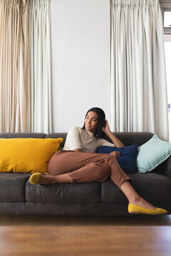Happy mixed race transgender woman relaxing in living room sitting on couch smiling