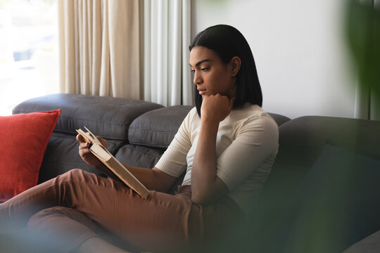 Mixed race transgender woman relaxing in living room sitting on couch reading book