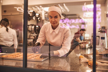 Energetic female confectioner arranging fresh macarons on tray