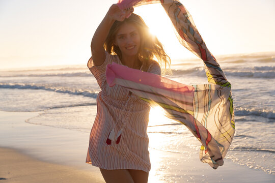 Portrait of caucasian woman holding scarf smiling while standing at the beach