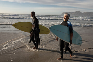 Happy senior african american couple carrying surf boards walking on the beach