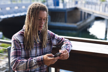 Mixed race man with dreadlocks standing outside cafe using smartphone