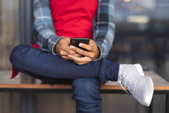 Mid section of mixed race male barista sitting on bench using smartphone