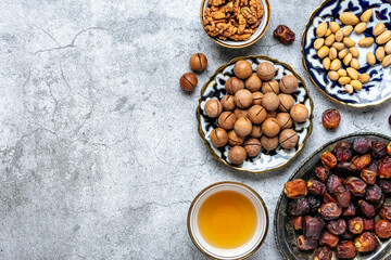 Popular food during Iftar - macadamia nuts, pistachios, walnuts, dry dates. Karan, rosary, teapot, bowl with black tea on concrete background Top view Flat lay Muslim holiday of holy month of Ramadan