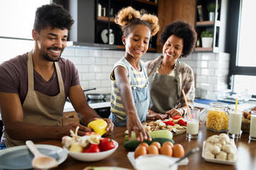 Happy girl and her beautiful parents are smiling while cooking in kitchen at home