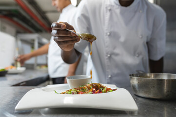 Midsection of mixed race professional chef finishing dish before serving