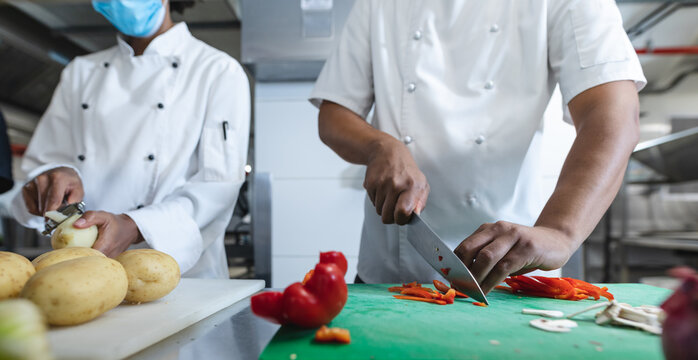 Midsection of diverce race professional chefs preparing vegetables wearing face masks