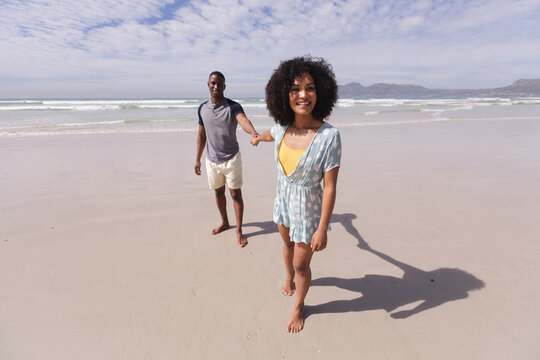 African american couple walking and holding hands at the beach smiling
