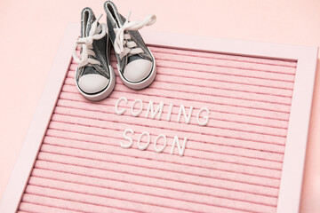 Waiting for labour, maternity concept. Coming soon words on pink frame with baby shoes