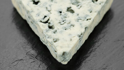 piece of blue cheese isolated on black stone plate, top view