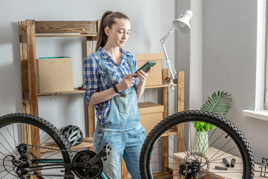 Woman is fixing a bicycle and using her phone. Concept of maintenance and preparation of the bike for the new season