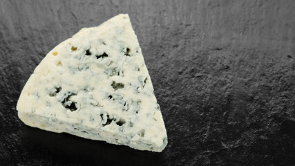 piece of blue cheese isolated on black stone plate, top view