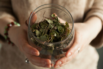 dried fragrant herbs in a glass jar, female hands hold a jar of herbs, medicinal herbal collection.