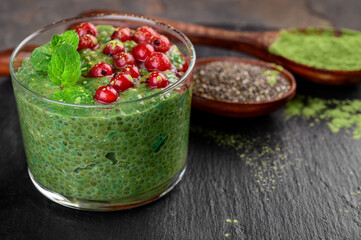 Matcha green tea chia seed pudding, dessert with fresh mint, berry and coconut on a black slate background