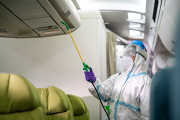 cleaning officer wearing ppe clean aircraft interior, passenger cabin and sprays disinfectant deep...