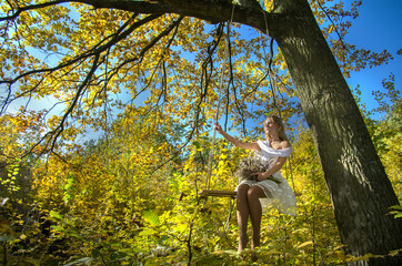 The girl is swinging on a swing in the autumn forest against the background of yellow-gold foliage. Selective focus.
