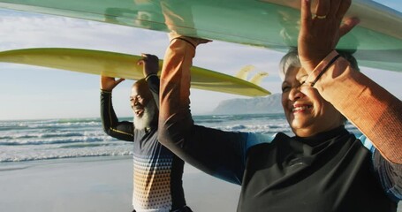 Senior african american couple walking with surfboards at the beach - Powered by Adobe