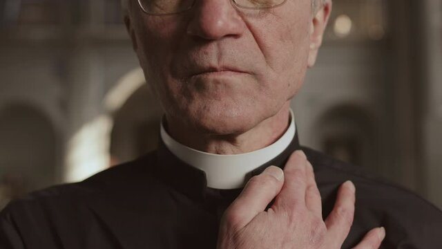 Close up of old Caucasian pastor wearing black shirt and white collar standing in Lutheran church and fixing his collar