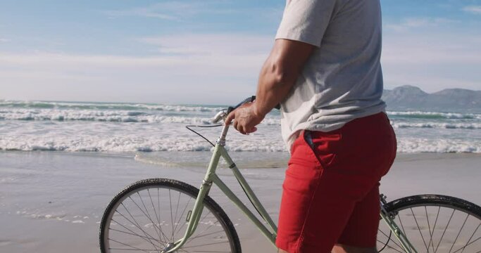 Senior african american man walking with a bicycle at the beach