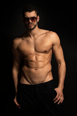 Fototapeta na wymiar Muscle strong beautiful stripped male model in black trousers wearing glasses eyewear on black isolated font background