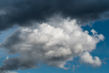 Naklejka na ściany i meble Dramatic sky, fluffy white cloud under dark cloud in blue sky
