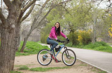 Fototapeta na wymiar beautiful athletic girl riding a bike, wearing jeans and a pink jacket, spring landscape