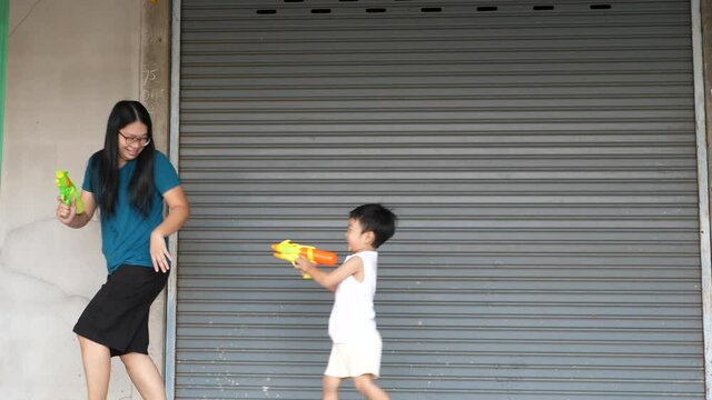 4K Asian Child Boy Playing Water Gun With Mother At Home In Songkran Day. Concept Of Happy Family Activity At Home, Freedom Fun, Togetherness. Songkran Festival Day 2021, New Normal Covid 19.