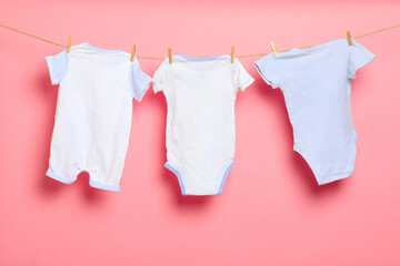 Baby clothes on a clothesline on pink background .