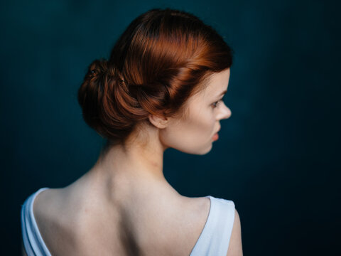 Portrait of a beautiful red-haired woman in a white dress on a dark background