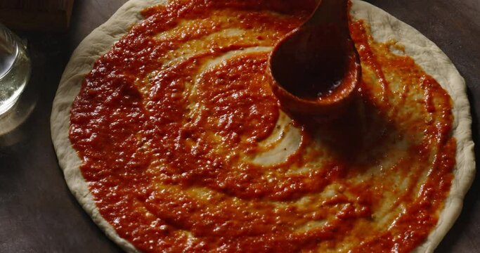 Chef is spreading  tomato sauce on pizza dough. Cooker making pizza with a traditional recipe in the kitchen, 4k footage