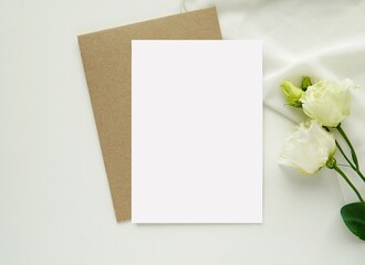 Wedding stationery mockup, empty greeting card, invitation for text or design, flat lay with brown envelope, white flowers and silk.
