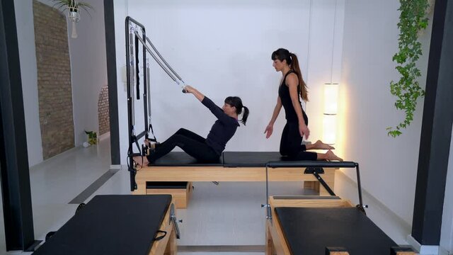 Woman doing exercises on pilates reformer with instructor