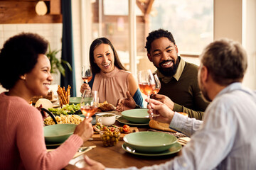 Happy black man having fun while talking with is friends during a meal at dining table.