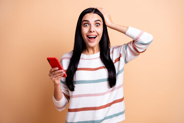 Photo of young crazy woman happy smile amazed shocked surprised use cellphone hand touch head isolated over beige color background