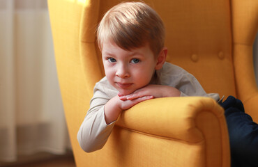 Little blond boy on the yellow armchair. International Children's Day.