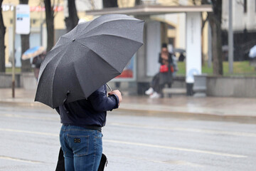 Heavy rain in city, man with umbrella standing on road background. Rainy weather, spring storm