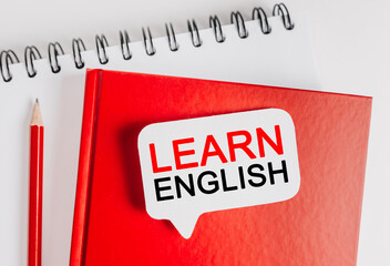 Text Learn ENGLISH a white sticker on red notepad with office stationery background. Flat lay on...