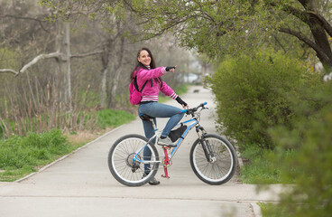 a sporty girl rides a bicycle on a pedestrian path , she saw something or someone, or teases, points with her hand