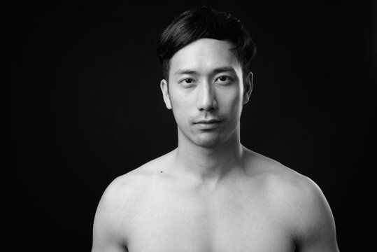 Young handsome Asian man shirtless against black background