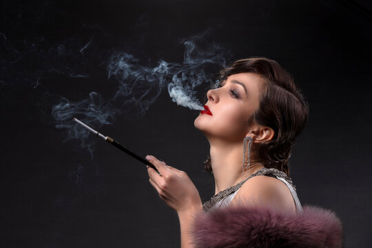 Retro woman portrait. A beautiful woman in the style of the 20s and 30s with a cigarette holder smokes.