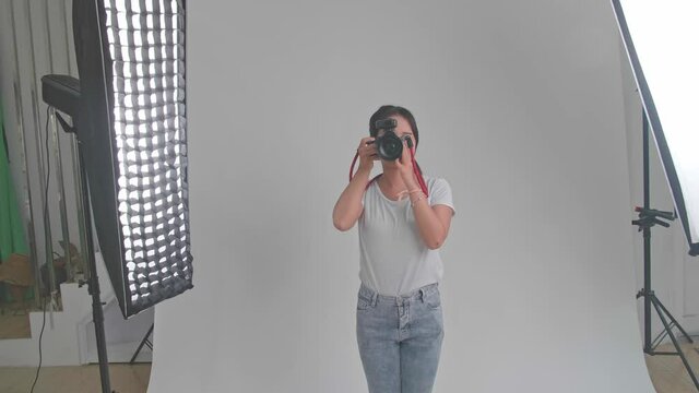 Young Asian Female Photographer Standing And Taking Photos In Studio
