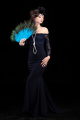 A beautiful girl dressed in the style of the 20-30s of the last century with a fan posing on a dark...