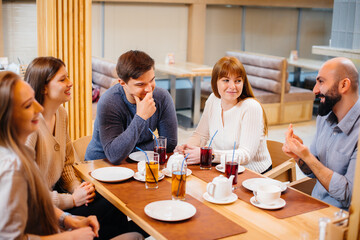 A group of young cheerful friends is sitting in a cafe talking and eating pizza. Lunch at the pizzeria.