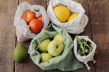 Obraz na płótnie Canvas Zero waste shopping. Apples, tomatoes, lemons, avocado, arugula in eco cotton bags on rustic wood