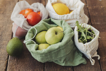 Fresh apples, tomatoes, lemons, avocado, arugula in eco cotton bags on rustic wood. Zero waste