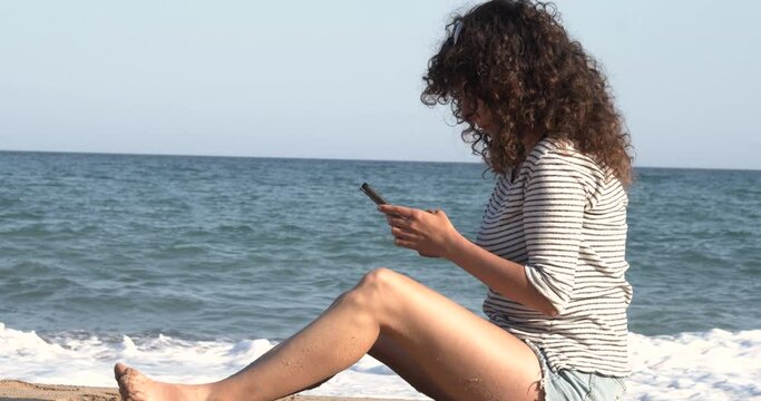 Woman chatting with a mobile phone on the beach while on vacation. Telephone communication, social networks