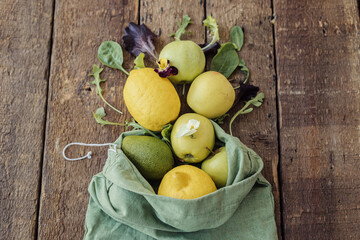 Fresh apples, lemon, avocado, salad leaves scattered from eco cotton bag on rustic wood top view