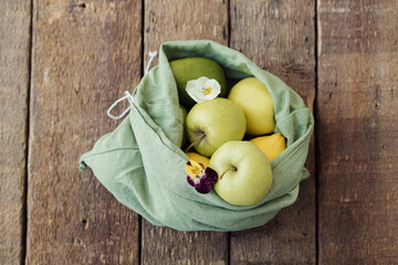 Fresh apples, avocado, lemons in eco cotton bag with flower on rustic wood. Zero waste shopping