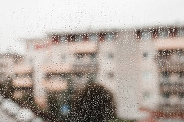 Drops of rain on a window pane with the blurred shapes of buildings, big city. Raindrops on window glass. Selective focus.