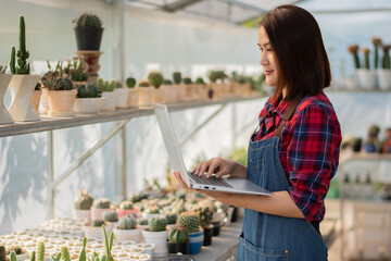 A beautiful Asian woman in a red and blue scottish shirt stands. holding a laptop On the farm cactus to accept orders for a cactus from an online market customer